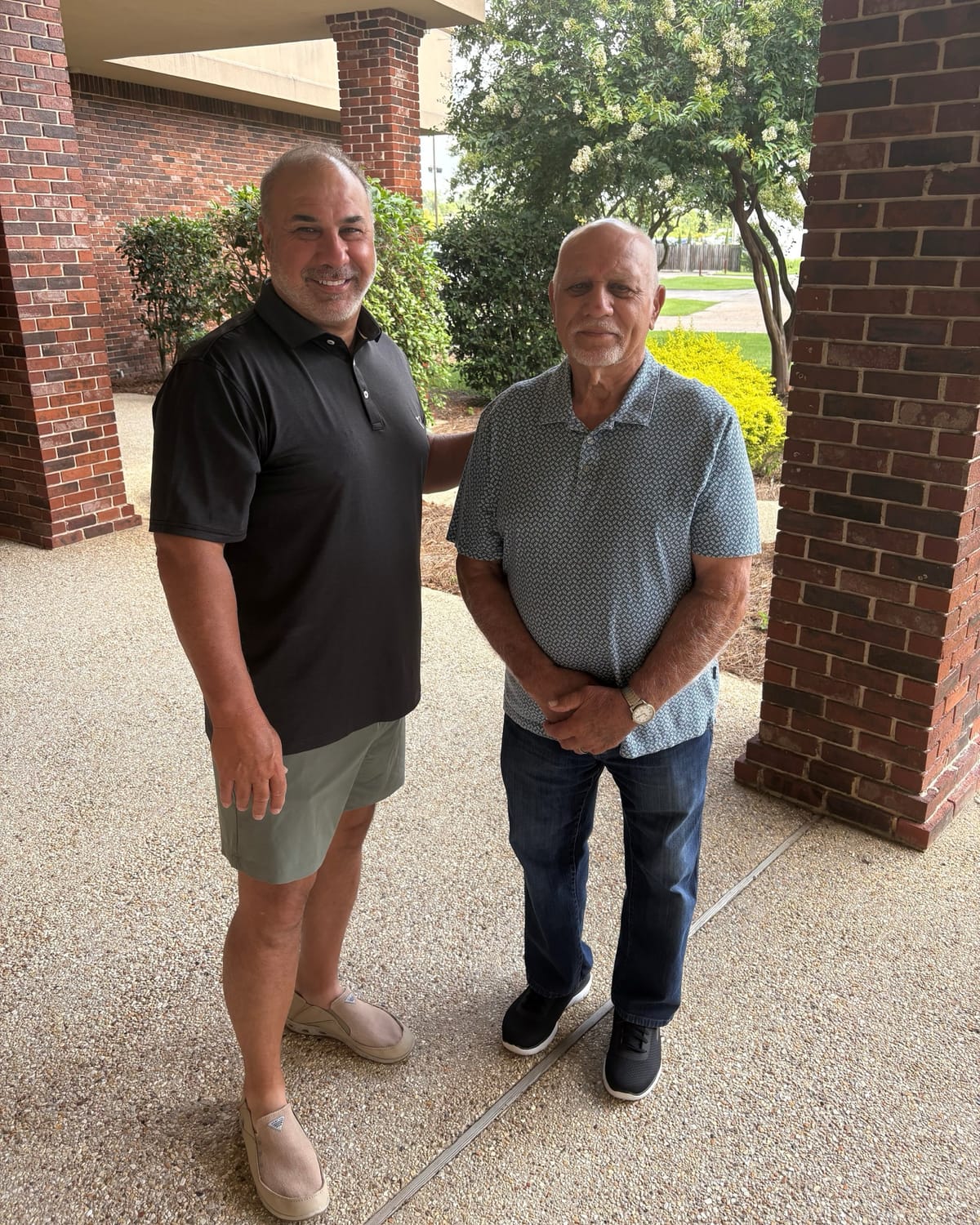 Joe Kent and Jimmy Joe Kent standing together under the brick portico at the Kent’s Plumbing campus in Walker, Louisiana